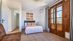 A bedroom with a bed, a brown leather sofa, a wooden door, and a window with curtains. - Villa "Can Antich" with Mountain View, Pool, Wi-Fi, Garden & Terrace (Lloseta)