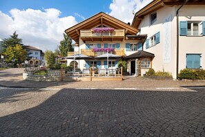 Un hotel con fachada de madera, un balcón con flores y un patio empedrado.