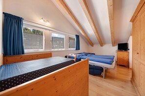 Una habitación con una litera, una cama individual, un armario de madera y una mesita pequeña.
