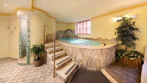 A spa area with a hot tub, stone steps, a potted plant, and a window with curtains.
