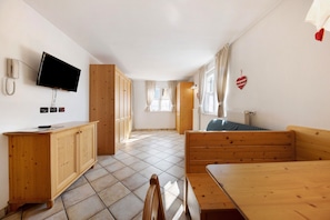 A room with a wooden cabinet, a television mounted on the wall, a wooden bench, and a table.