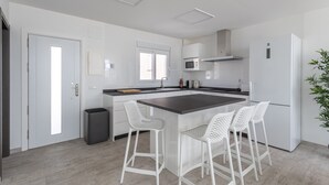 A modern kitchen with white cabinets, a central island with bar stools, a microwave, and a refrigerator. - Holiday Apartment "Nerja Luxury" with Sea View, Terrace & Wi-Fi (Nerja)