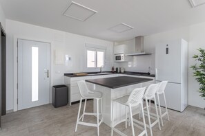 A modern kitchen with white cabinets, a central island with bar stools, a microwave, and a refrigerator.