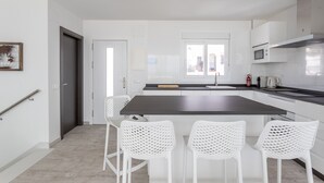 A modern kitchen with white cabinetry, a central island with bar stools, a microwave, and a window. - Holiday Apartment "Nerja Luxury" with Sea View, Terrace & Wi-Fi (Nerja)