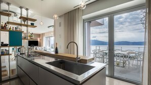 A modern kitchen with a large island, a built-in sink, and a view of the outdoors. - Exclusive Villa Agave with Lake & Mountain View, Pool, Whirlpool, and Sauna (Toscolano-Maderno)