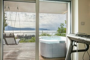 A balcony with a hot tub, a swing chair, and a view of a lake and mountains.