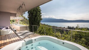 A balcony with a hot tub, lounge chairs, and a view of a lake and mountains. - Exclusive Villa Agave with Lake & Mountain View, Pool, Whirlpool, and Sauna (Toscolano-Maderno)