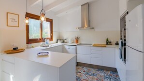 A modern kitchen with white cabinetry, a central island, a stainless steel range hood, and a refrigerator. - Vacation Villa "Villa Diani" with Pool, Wi-Fi, Garden & Terrace (Binibequer)