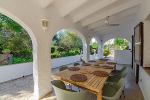 A covered outdoor dining area with a long table, chairs, and a ceiling fan.