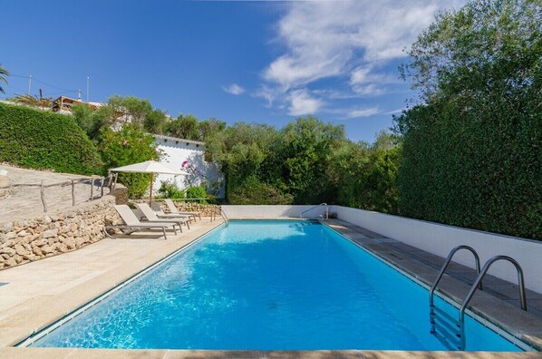 A rectangular swimming pool with a metal ladder, surrounded by a stone wall and a white fence.