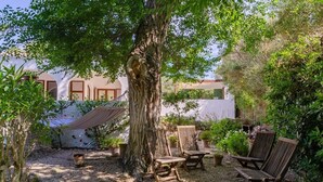 A garden with a large tree, wooden chairs, and potted plants. - Vacation Villa "Villa Diani" with Pool, Wi-Fi, Garden & Terrace (Binibequer)