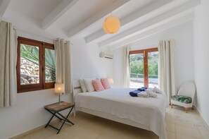 A bedroom with a bed, a bedside table with a lamp, a chair, and a view of greenery outside.