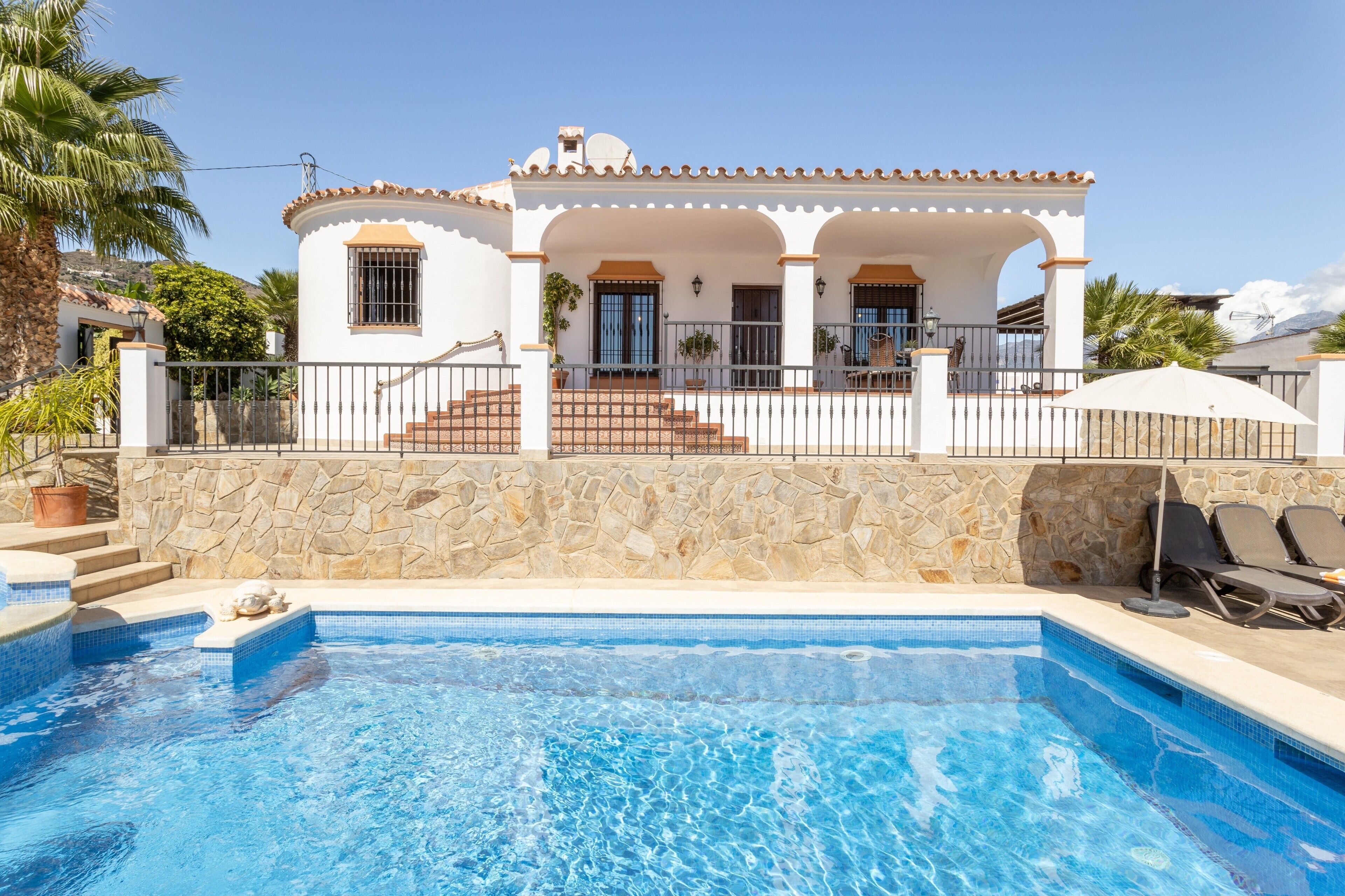 Vista della piscina e di una casa con un muro in pietra, una piscina e un patio con sedie.