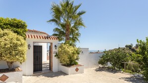 A building with a tiled roof, a door, and a small garden area with a palm tree and shrubs. - Villa "Natalia" with Sea & Mountain View, Private Pool, Air Conditioning & Terrace (Nerja)