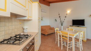 A kitchen with a gas stove, white cabinets with yellow trim, a dining table with chairs, a sofa, and a television.