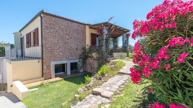 A stone building with a balcony, a stone pathway, and pink flowers.