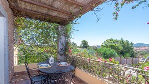 A covered outdoor dining area with a table and chairs, a pergola, and a view of greenery and hills.