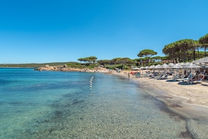 Ein Strand mit klarem Wasser, Sonnenschirmen und Bäumen.