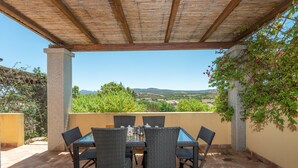 Eine Terrasse im Freien mit Tisch und Stühlen, einer Pergola und Blick auf die Landschaft.