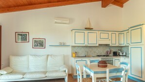 Una cocina con armarios blancos, una mesa de comedor con sillas, un sofá y una pequeña decoración de velero.