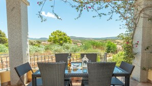 Un patio con sillas de mimbre y una mesa, con vistas a un paisaje pintoresco.