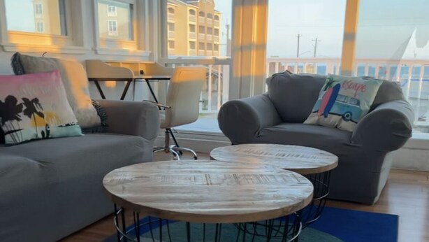 Ein modernes Wohnzimmer mit zwei grauen Sofas, einem runden Couchtisch mit Drahtgestell und Blick auf ein Gebäude durch große Fenster.
