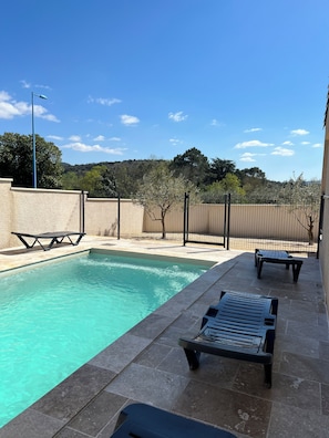A swimming pool with lounge chairs and a picnic table, surrounded by a fence and trees.