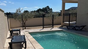 Una piscina con sillones de descanso, una valla y un edificio al fondo.