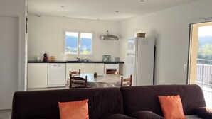 Una sala de estar moderna con un conjunto de sofá marrón, una mesa de centro de vidrio y vistas a una cocina y zona de comedor.