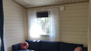 Una habitaci ón con un sofá seccional azul oscuro, una ventana con cortinas de gasa y piso de madera.