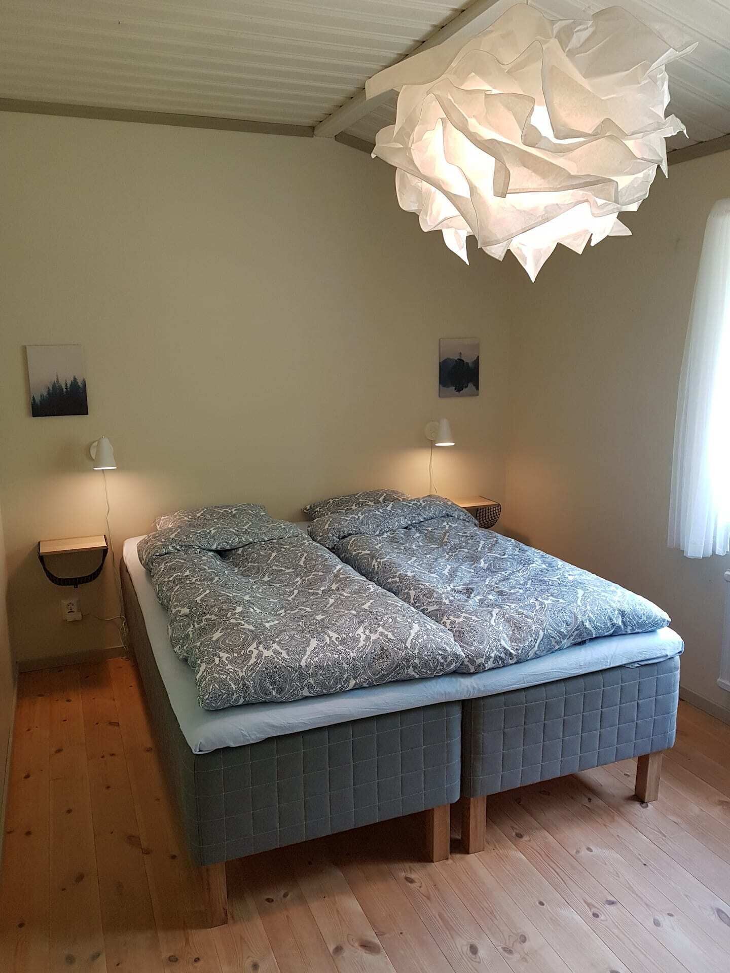 A bedroom with a bed, two bedside tables, a hanging light fixture, and two wall-mounted lamps.