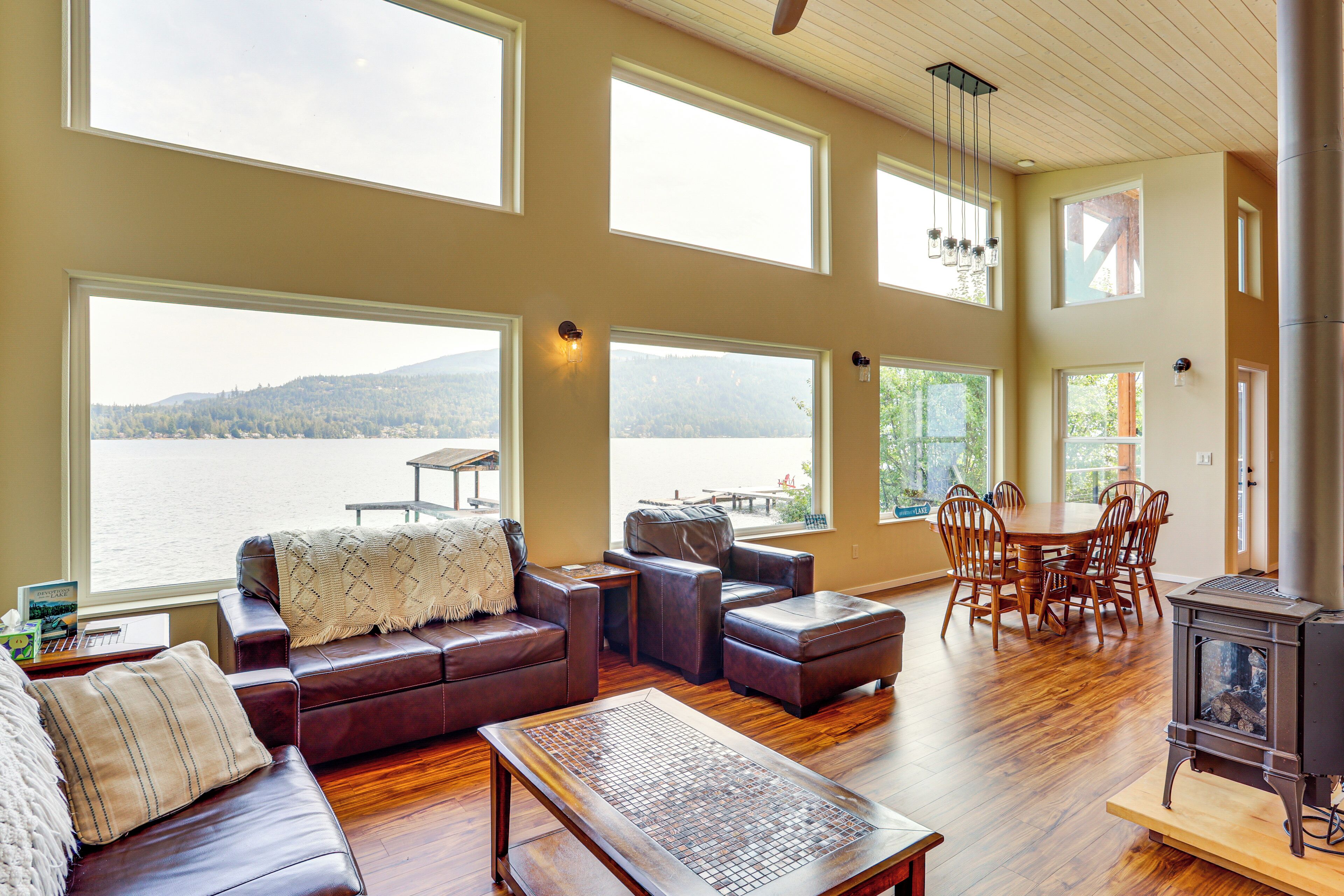 A spacious living room with a large window overlooking a lake, a cozy seating area, and a dining table with chairs.