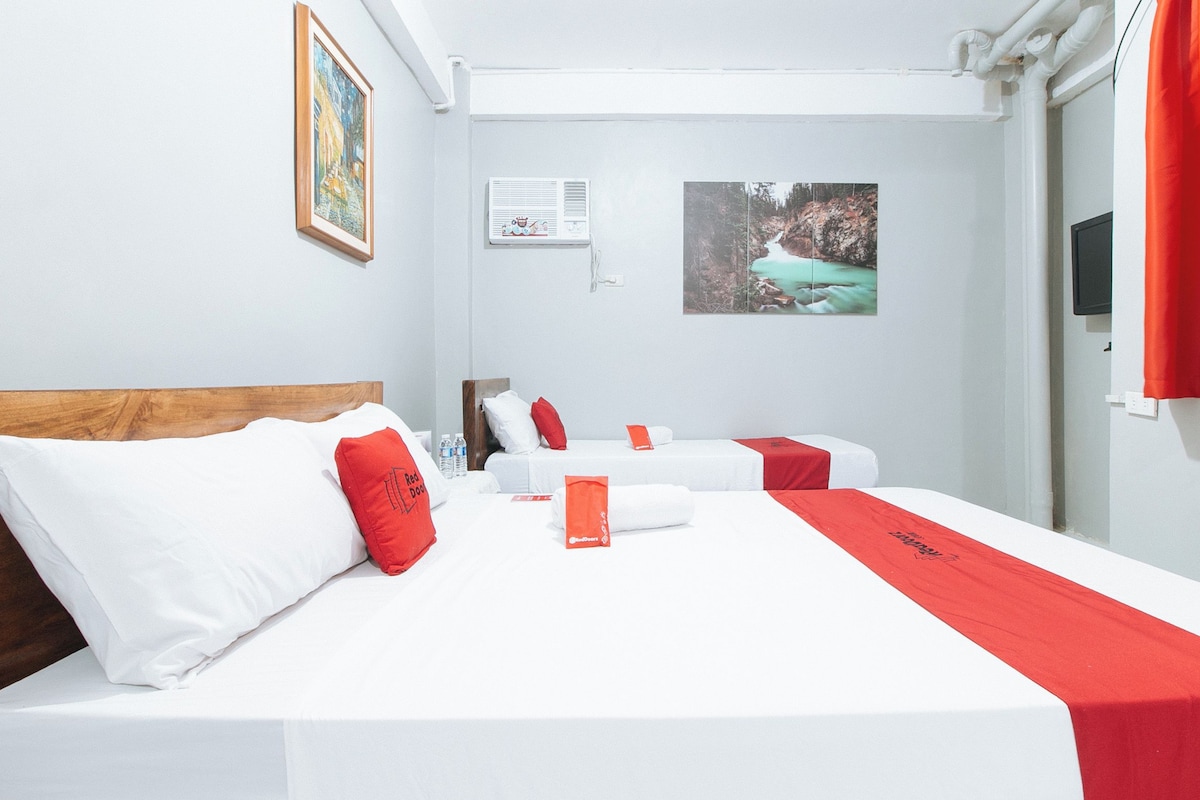 Habitación de hotel con una cama grande, dos camas más pequeñas, un cuadro, un equipo de aire acondicionado y una ventana con cortinas.