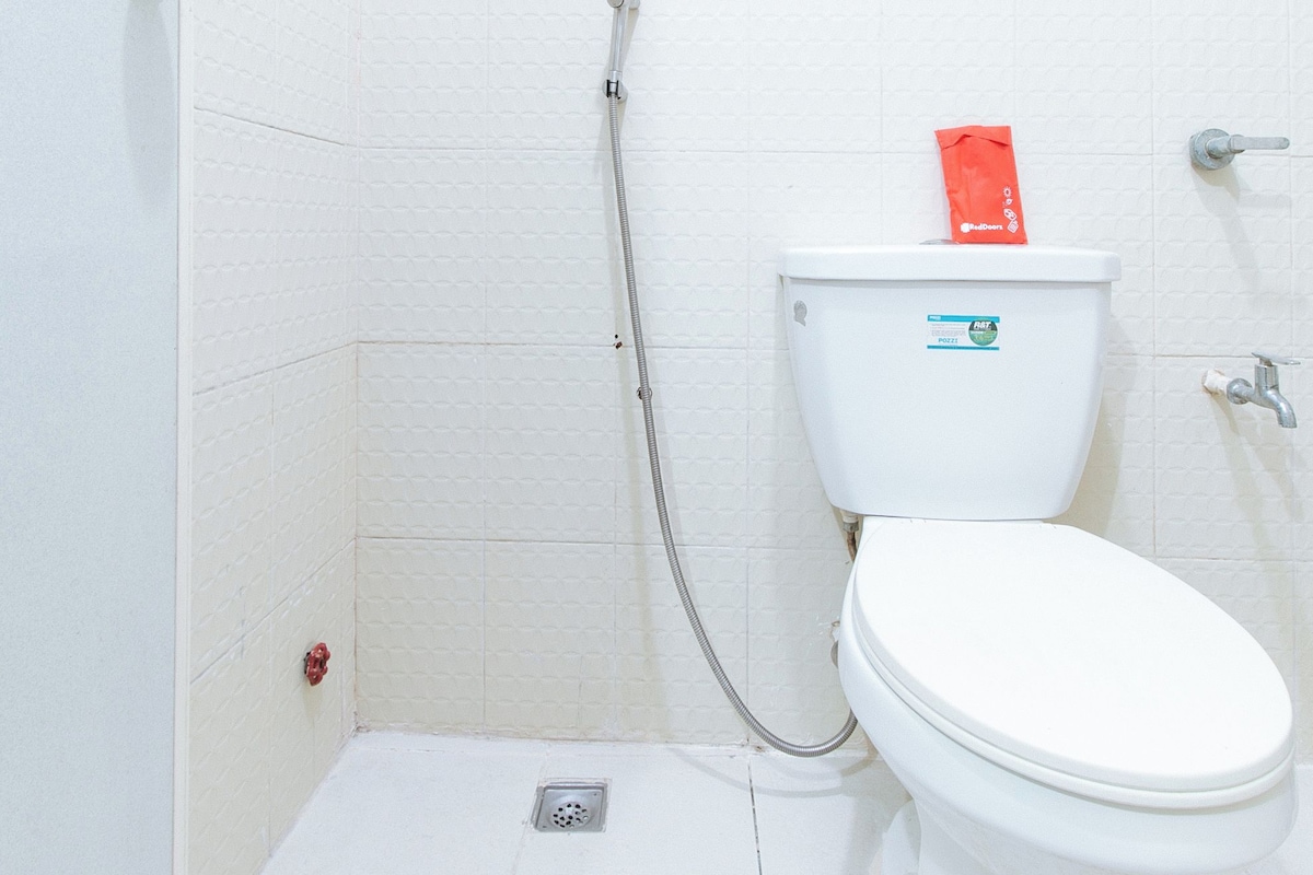 Un inodoro blanco con un accesorio bidé y un paquete rojo encima.
