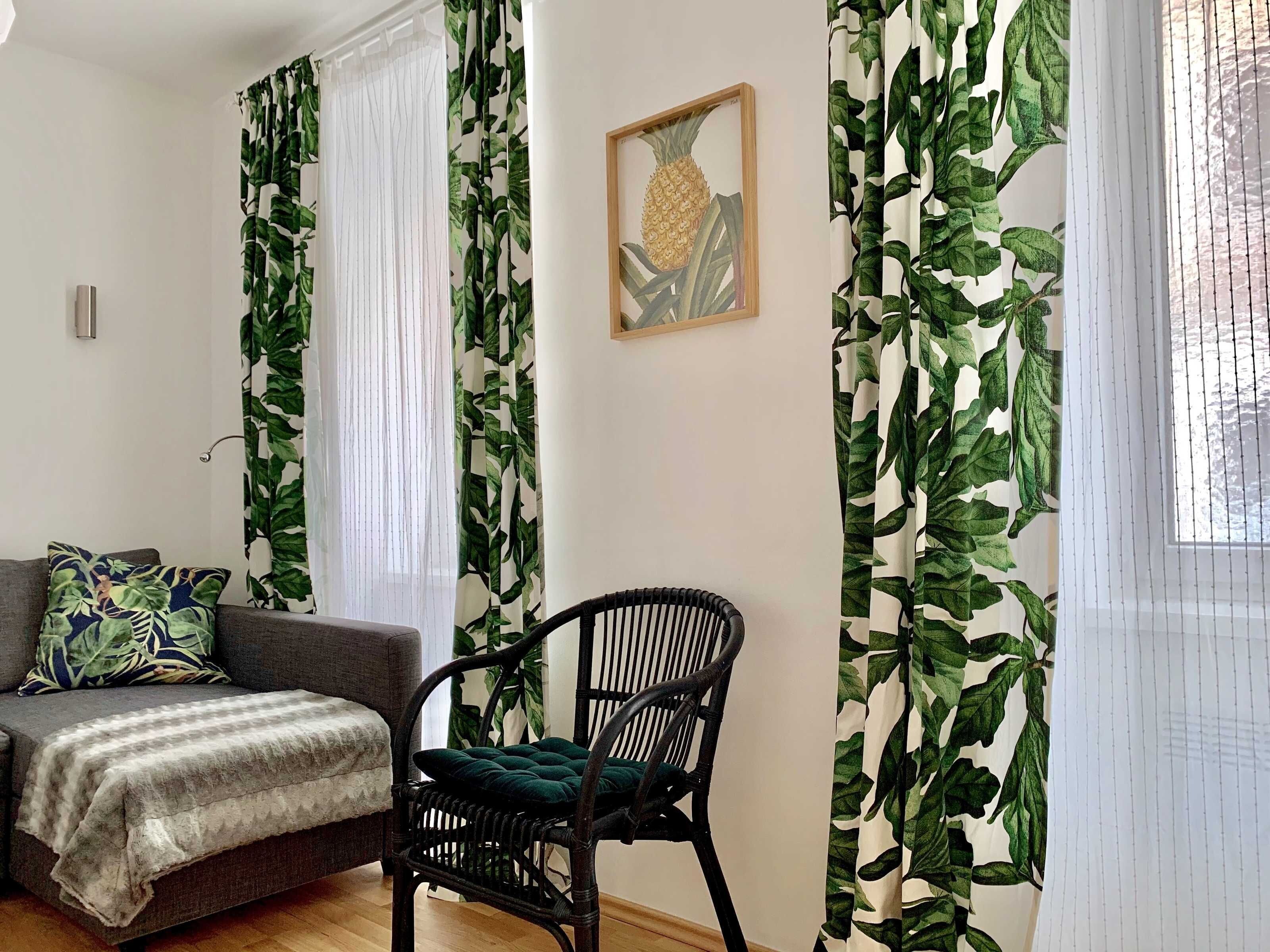 A living room with a sofa, a chair, and curtains with a leaf pattern.
