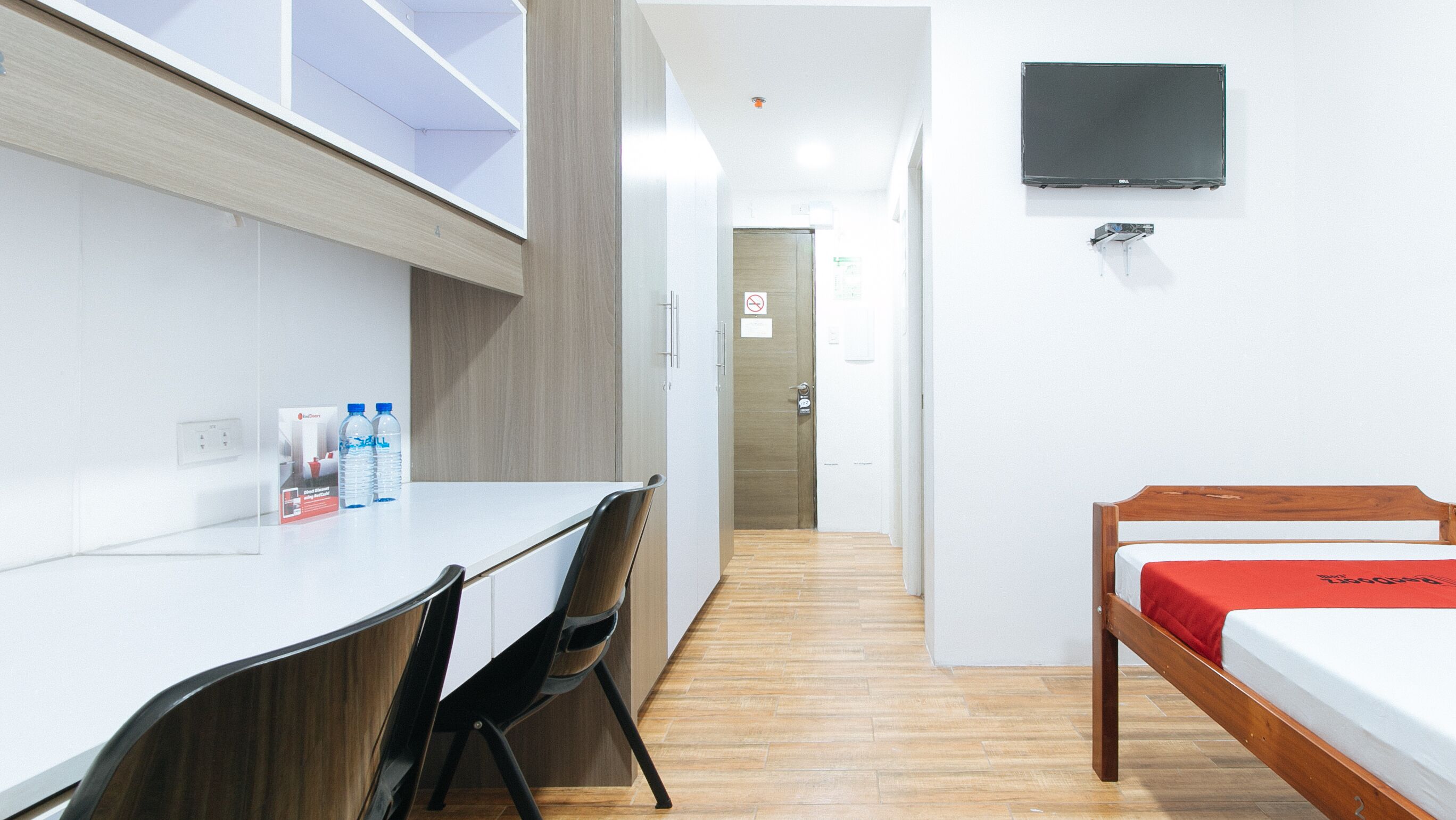 A hotel room with a bed, a desk with chairs, a TV mounted on the wall, and a water dispenser on the desk.