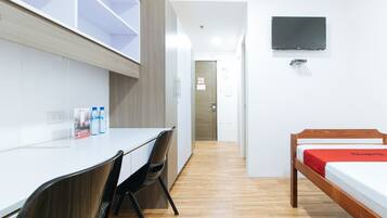 A hotel room with a bed, a desk with chairs, a TV mounted on the wall, and a water dispenser on the desk.