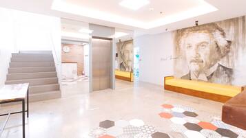 A modern lobby with a staircase, a reception desk, and a large mural.