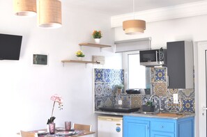 A kitchen with a microwave, sink, and blue cabinets. There are hanging lights and a small shelf with flowers.