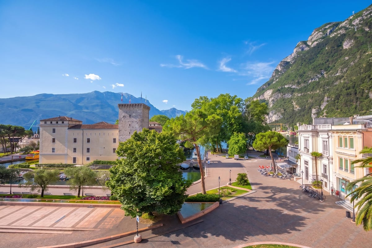 Une place avec une fontaine, un bâtiment qui ressemble à un château et une montagne en arrière-plan.