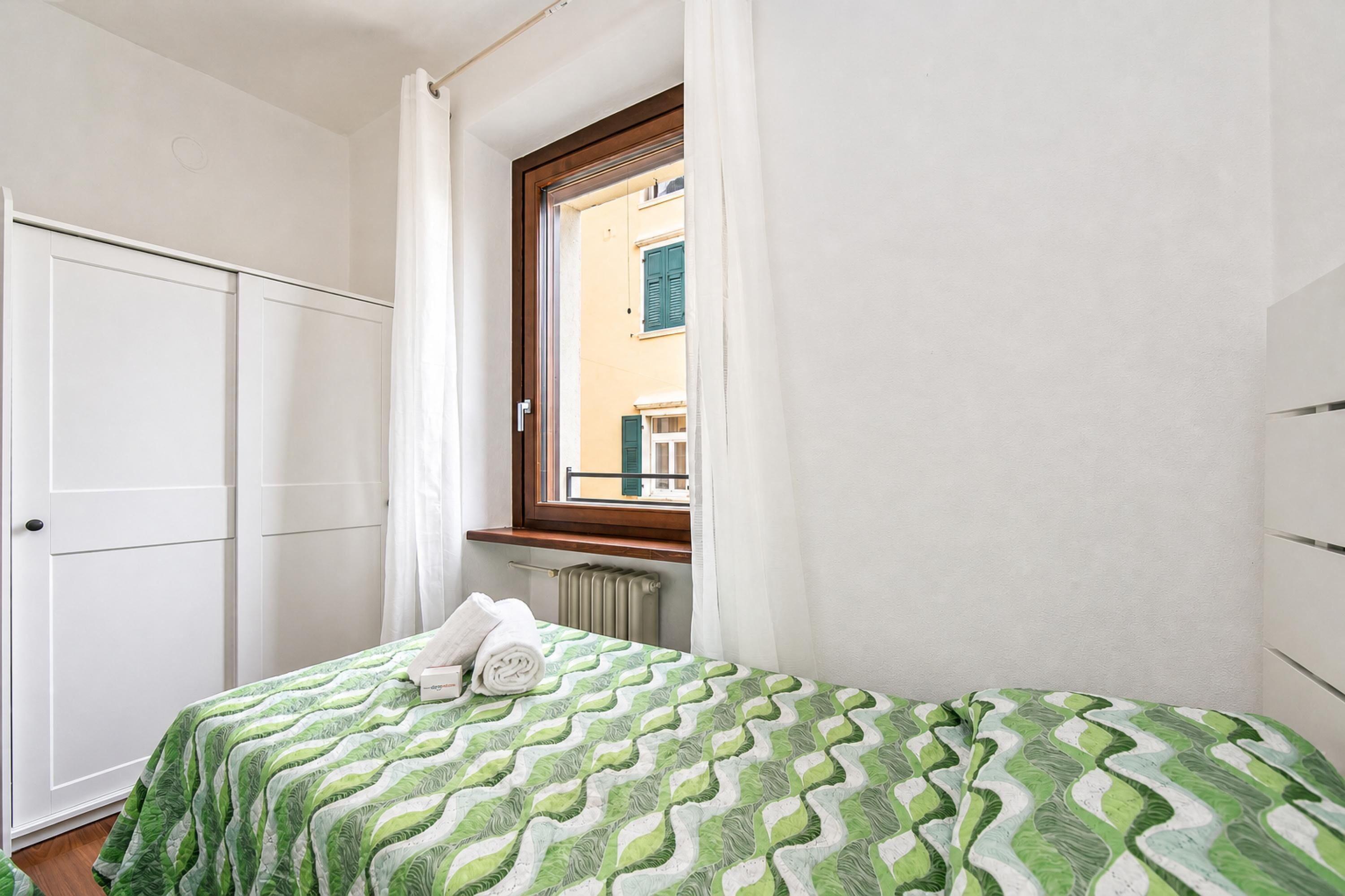 A bedroom with a bed, a window, a radiator, and a wardrobe.