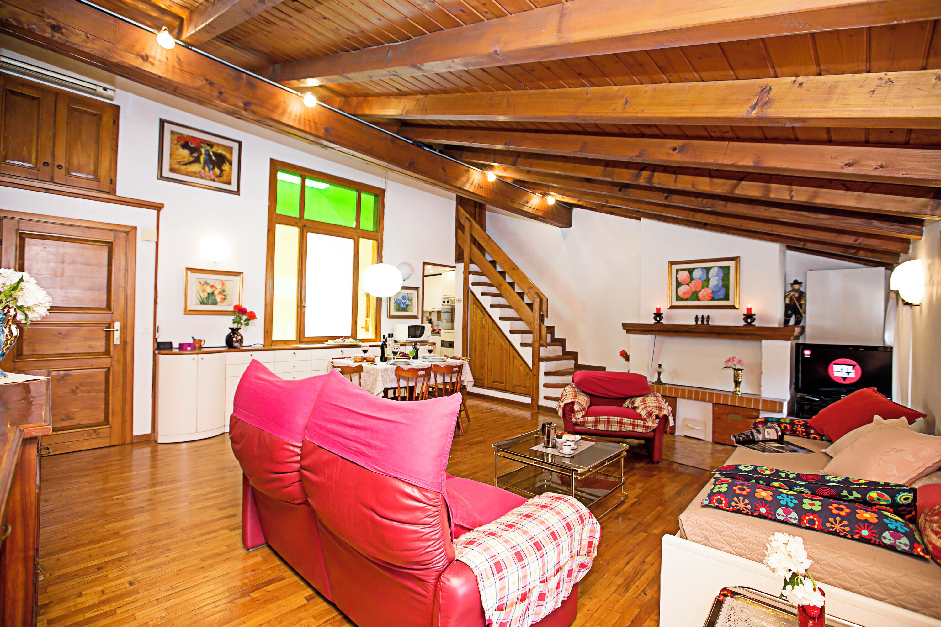Un salon chaleureux avec un canapé rouge, une table basse et un escalier menant à un niveau supérieur.