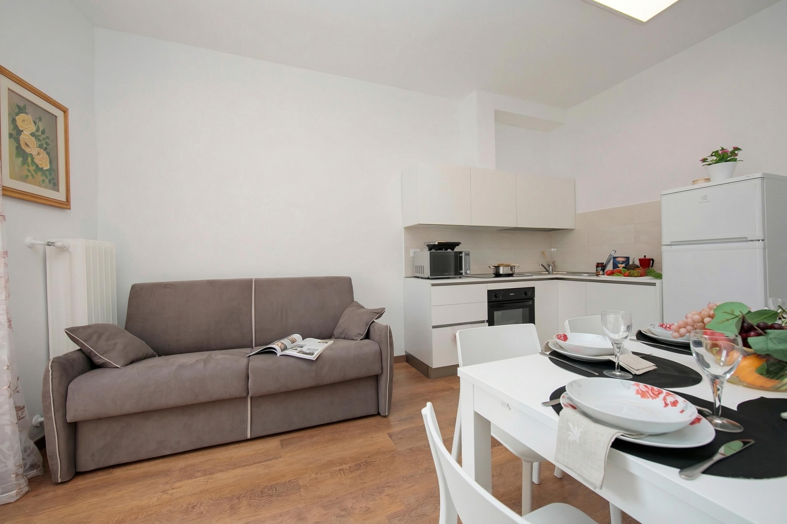 A modern living room with a sofa, a dining table set for two, and a kitchen area with appliances.