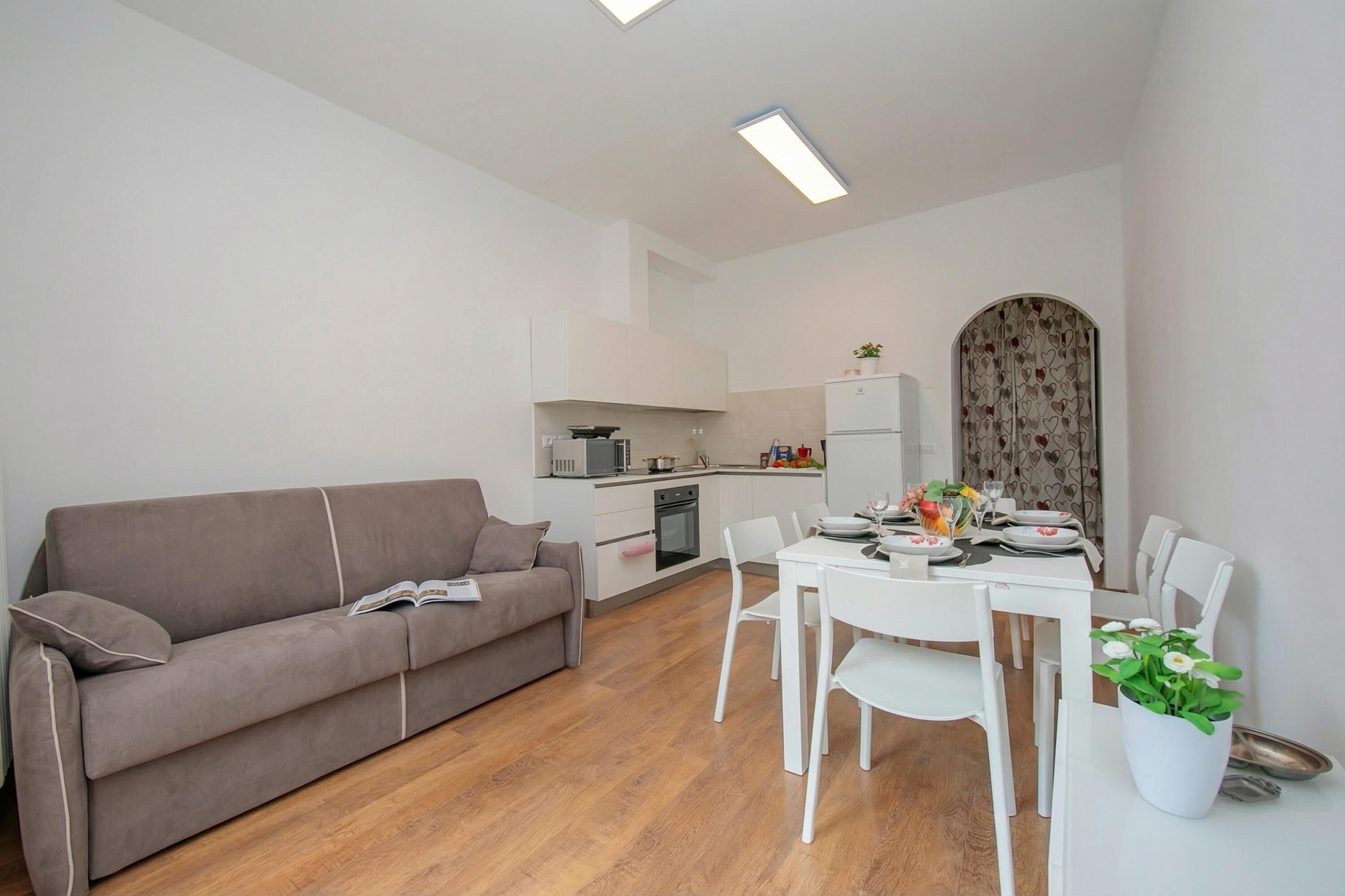 Una sala de estar moderna con sofá, mesa de comedor, sillas y una cocina al fondo.