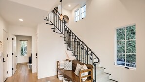 A staircase with a wrought iron railing, a wooden bench with cushions, and a view of the outdoors through a window. - "Casa Playa" in the heart of West Beach - impeccably remodeled, with A/C and 2 car garage! (Santa Barbara)