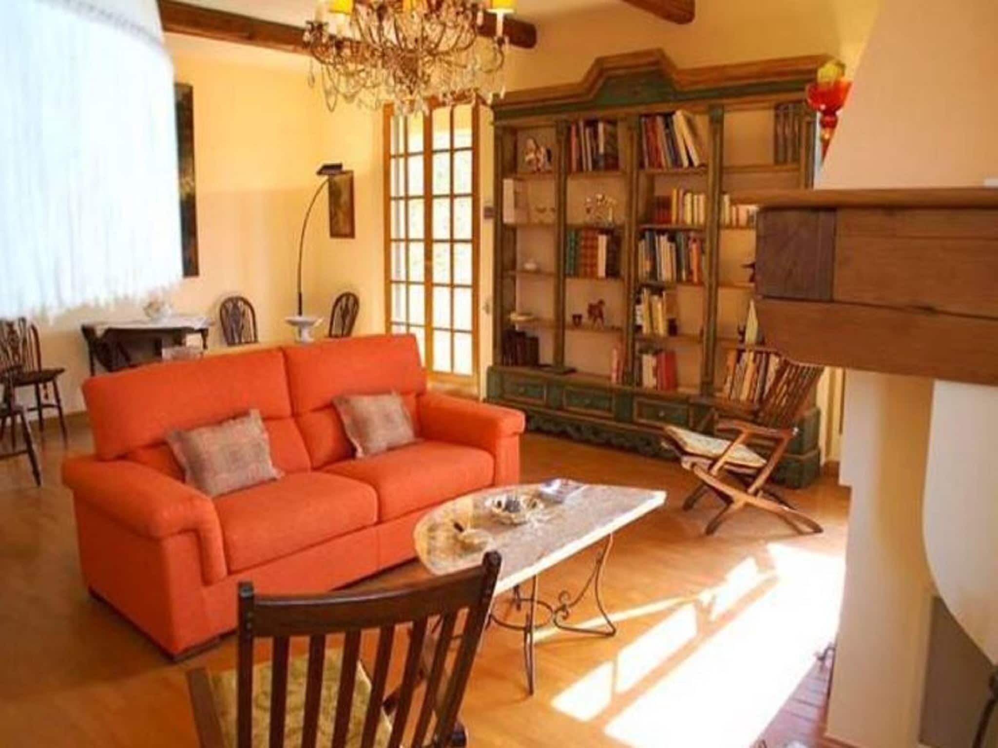 Ein gemütliches Wohnzimmer mit einem hellorangefarbenen Sofa, einem Holztisch und einem Bücherregal voller Bücher.