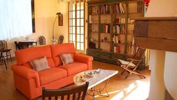 Ein gemütliches Wohnzimmer mit einem hellorangefarbenen Sofa, einem Holztisch und einem Bücherregal voller Bücher.