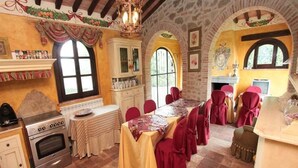 A rustic dining area with a long table, red chairs, and a stone wall.