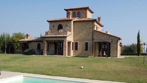 A stone villa with a swimming pool, a lawn, and a tennis court.