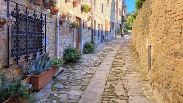 A narrow cobblestone street lined with stone buildings, some with balconies and potted plants. - Stone house villa with Spa in Cortona (Cortona)